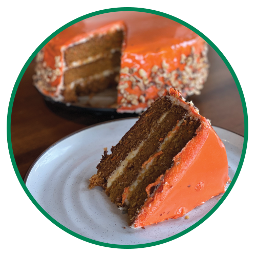 Slice of carrot cake on white plate with the rest of the cake in the background