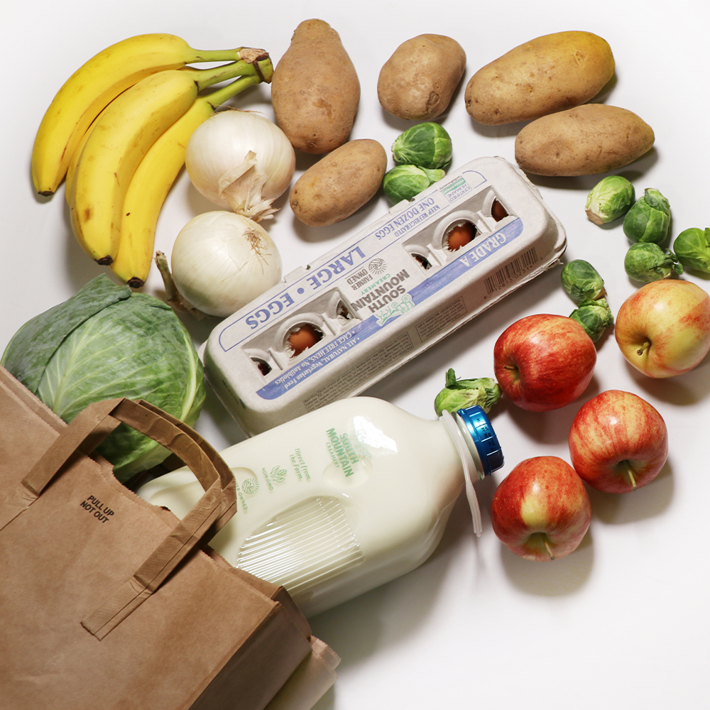 Top-down photo shows produce, eggs, and SMC milk spilling out of a brown paper grocery bag