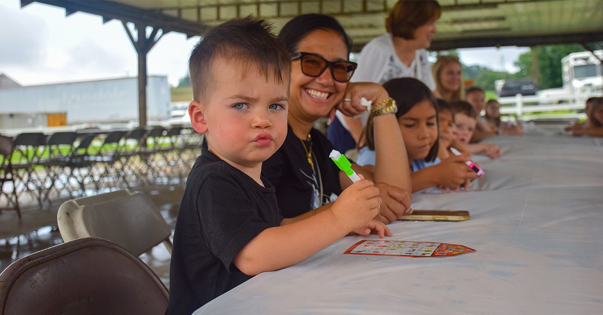 Young child coloring at a table outdoors under a tent